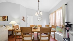 Un comedor con sillas de madera y una mesa, una lámpara, un reloj y una ventana con cortinas.