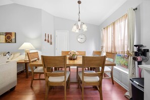 Ein Essbereich mit Holzbänken und einem Tisch, einer Lampe, einer Uhr und einem Fenster mit Vorhängen.
