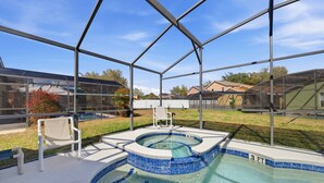 Una piscina techada con un jacuzzi, rodeada por una estructura de metal y paneles de vidrio, ubicada en una zona residencial.
