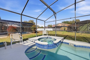 Ein überdachter Pool mit Whirlpool, umgeben von einer Metallkonstruktion und Glasscheiben, in einer Wohngegend gelegen.