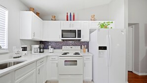 Cocina moderna con armarios blancos, microondas, estufa y refrigerador.
