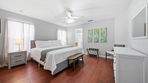 Un dormitorio con cama, mesita de noche, banco, cómoda y una obra de arte en la pared.