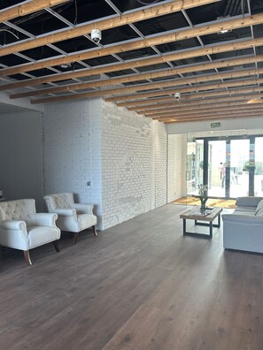 Een ruime lobby met een hoge plafond, zichtbare houten balken, witte bakstenen muren en een zithoek met witte gestoffeerde stoelen.