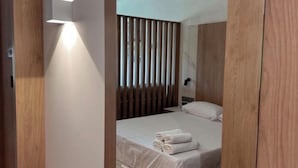 A modern bedroom with a large mirror, wooden paneling, a bed with white linens, and a bedside table. - Tudcon Palm (Madrid)