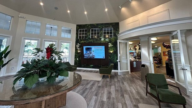Eine geräumige Lobby mit einer großen Anzeige, die Parkinformationen zeigt, einer Sitzecke mit Glastisch und Blick ins Freie durch große Fenster.