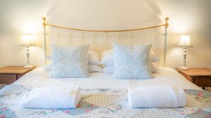 Un lit bien fait, recouvert d’une courtepointe à motifs floraux, avec deux lampes de chevet et une tête de lit ornée d’un cadre doré.