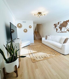 A modern living room with a flat-screen TV, a white sofa, a world map wall, a staircase, and a potted plant.