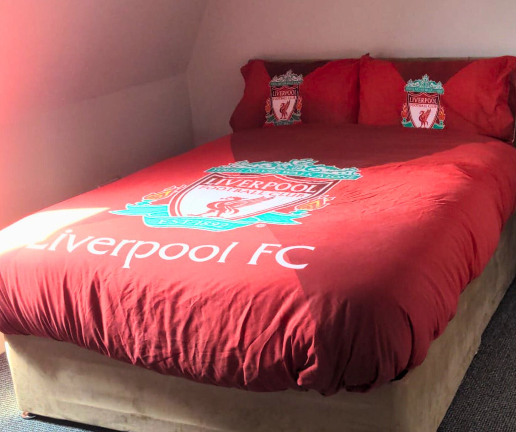 Una cama con un edredón rojo con el logotipo del Liverpool FC.