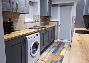 A compact kitchen with grey cabinets, a washing machine, a toaster, and a sink. - The Red Lounge Rooms Near Anfield (Liverpool)