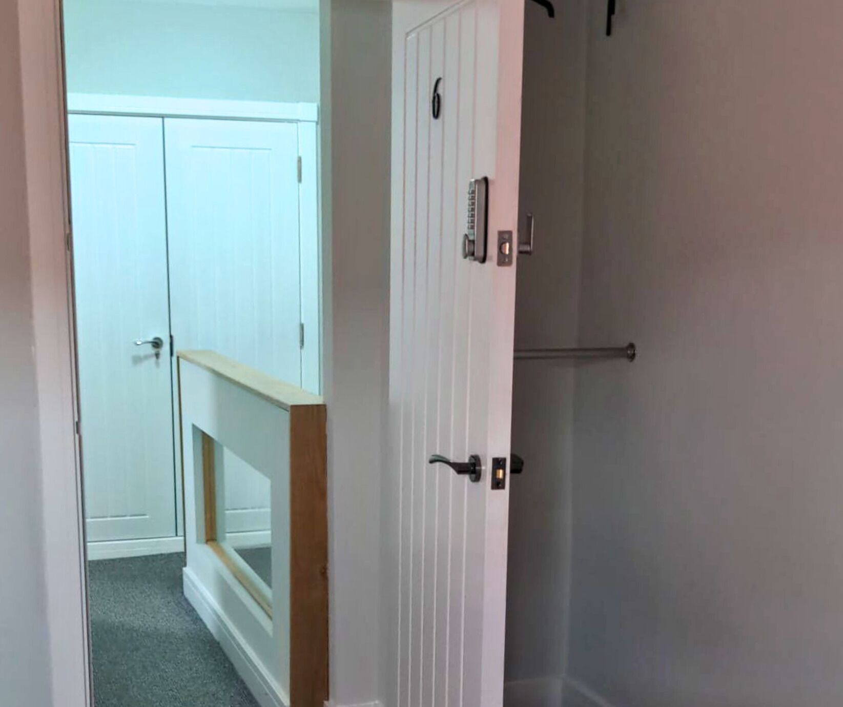 Un couloir avec une porte blanche, une main courante en bois et une armoire blanche avec une porte.