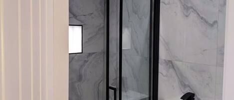 Un baño moderno con cabina de ducha de vidrio, un lavabo blanco y baldosas de mármol.
