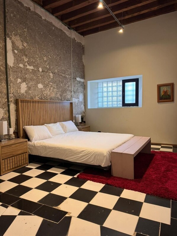 Una camera da letto con pavimento a scacchi, un letto con testiera in legno, una finestra vista e un tappeto rosso.