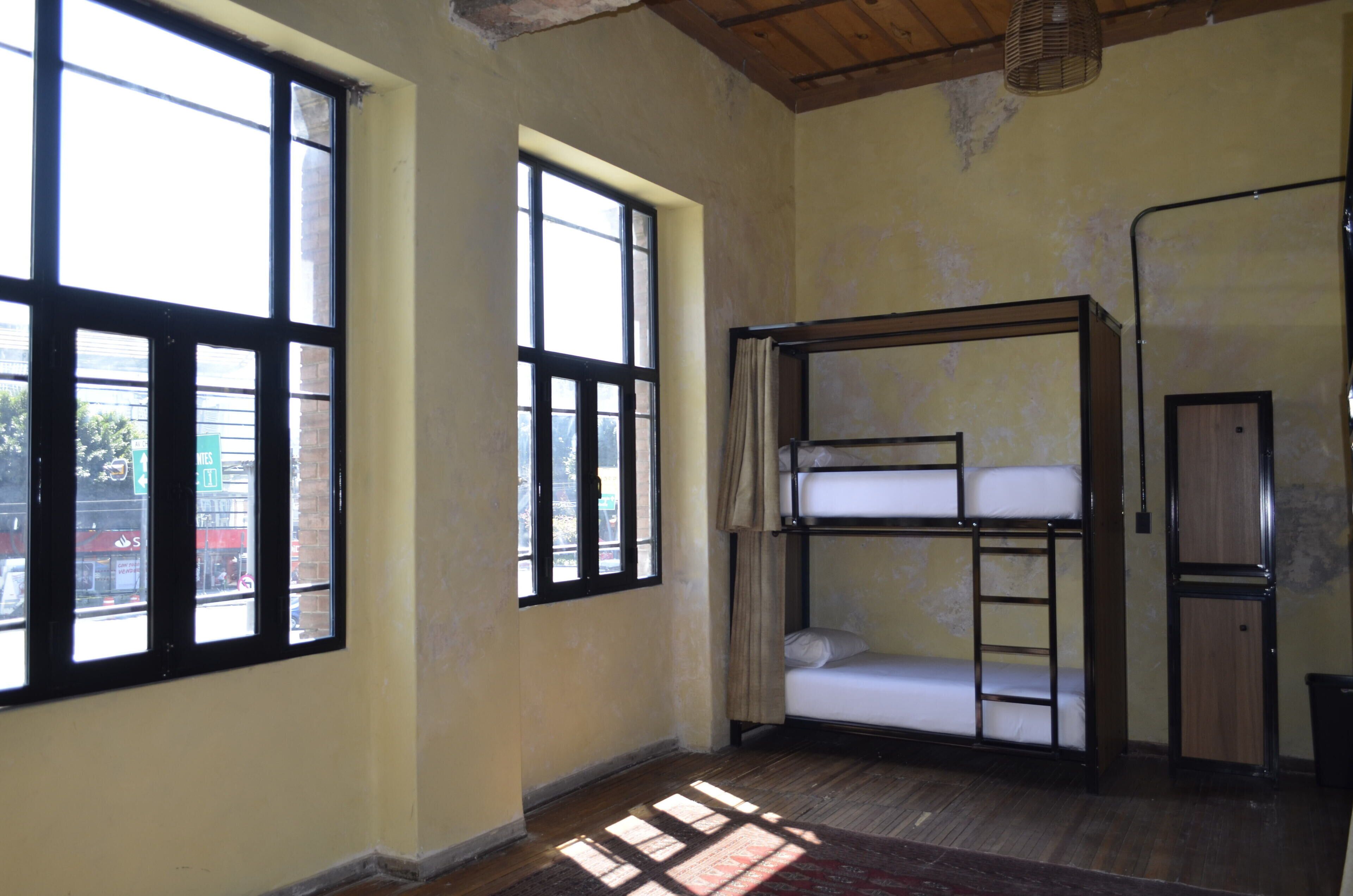Ein Zimmer mit Etagenbetten, großen Fenstern und einer Holzbalkendecke.