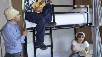 A bunk bed with two people, one playing guitar and another reading a book.