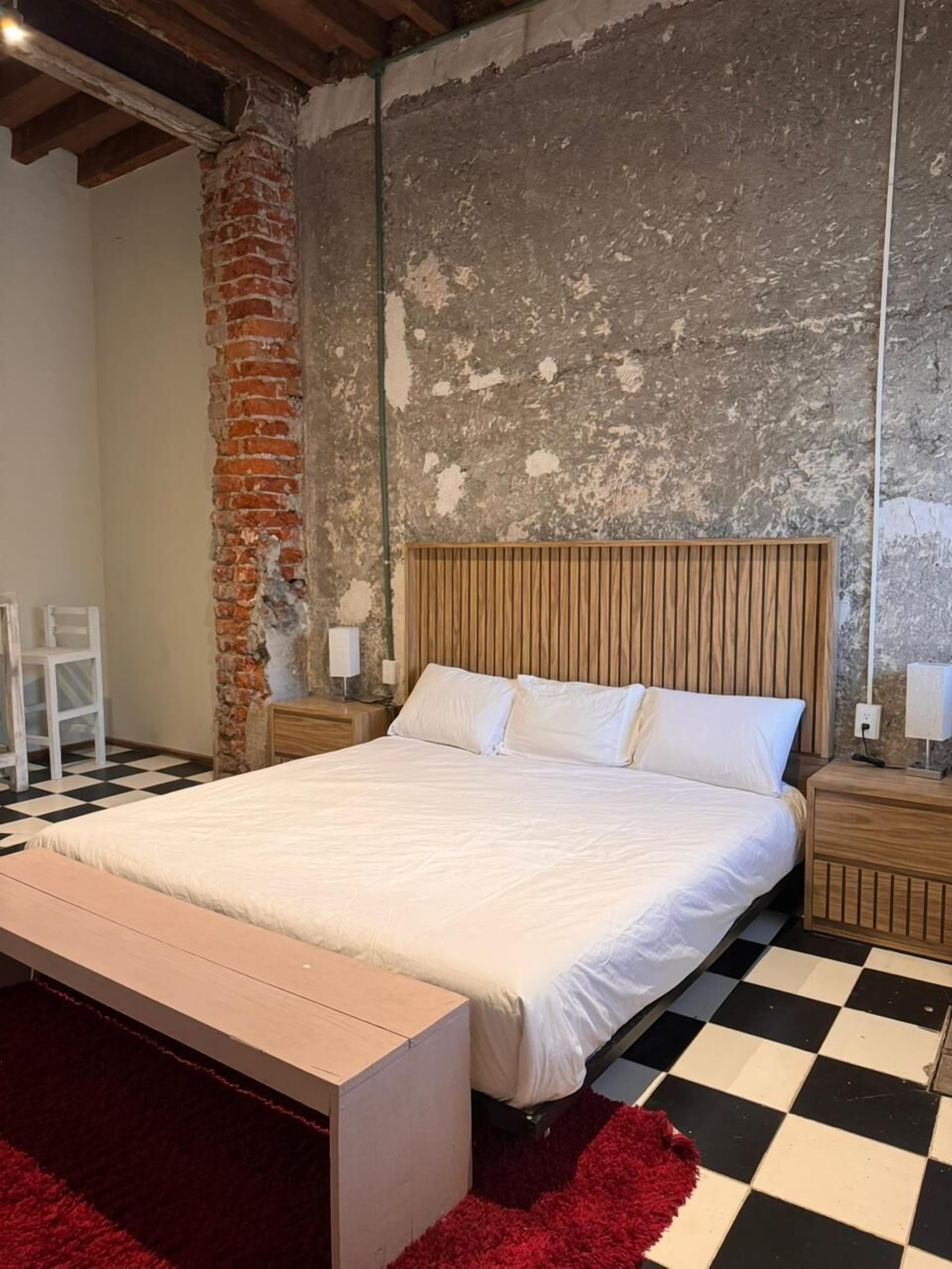 A bedroom with a large bed, a wooden headboard, a red rug, and a checkered floor.