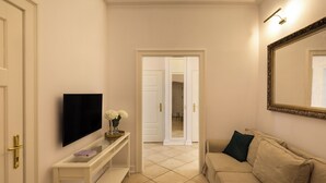 En hall med en tv placerad på en vit tv-bänk, en beige soffa med en spegel och en dörr som leder till ett annat rum.