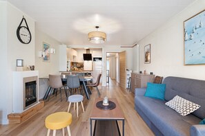 A modern living room with a fireplace, a dining area, a kitchen, and a sofa with cushions. - Apartment 'Les Gemaux 2' in Villard-de-Lans, 6 Guests, 1 Main Bedroom and Cabin Room (Villard-de-Lans)