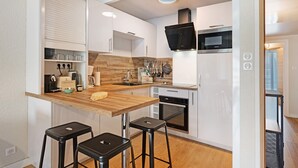 A compact kitchen with a wooden countertop, a microwave, an oven, and a sink. There are two black stools and a wooden bar stool. - Apartment 'Les Gemaux 2' in Villard-de-Lans, 6 Guests, 1 Main Bedroom and Cabin Room (Villard-de-Lans)