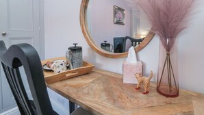 A wooden console table with a mirror, a vase with pink feathers, a ceramic pig figurine, and a small animal figurine. - Cuckoo's Nest (Whitby)