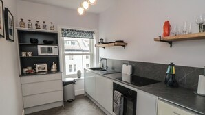 A modern kitchen with a microwave, oven, and sink. There are shelves with bottles and a window with a view. - Cuckoo's Nest (Whitby)