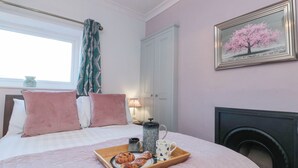 A bedroom with a bed, pillows, a tray with pastries, a coffee pot, and a framed picture on the wall. - Cuckoo's Nest (Whitby)