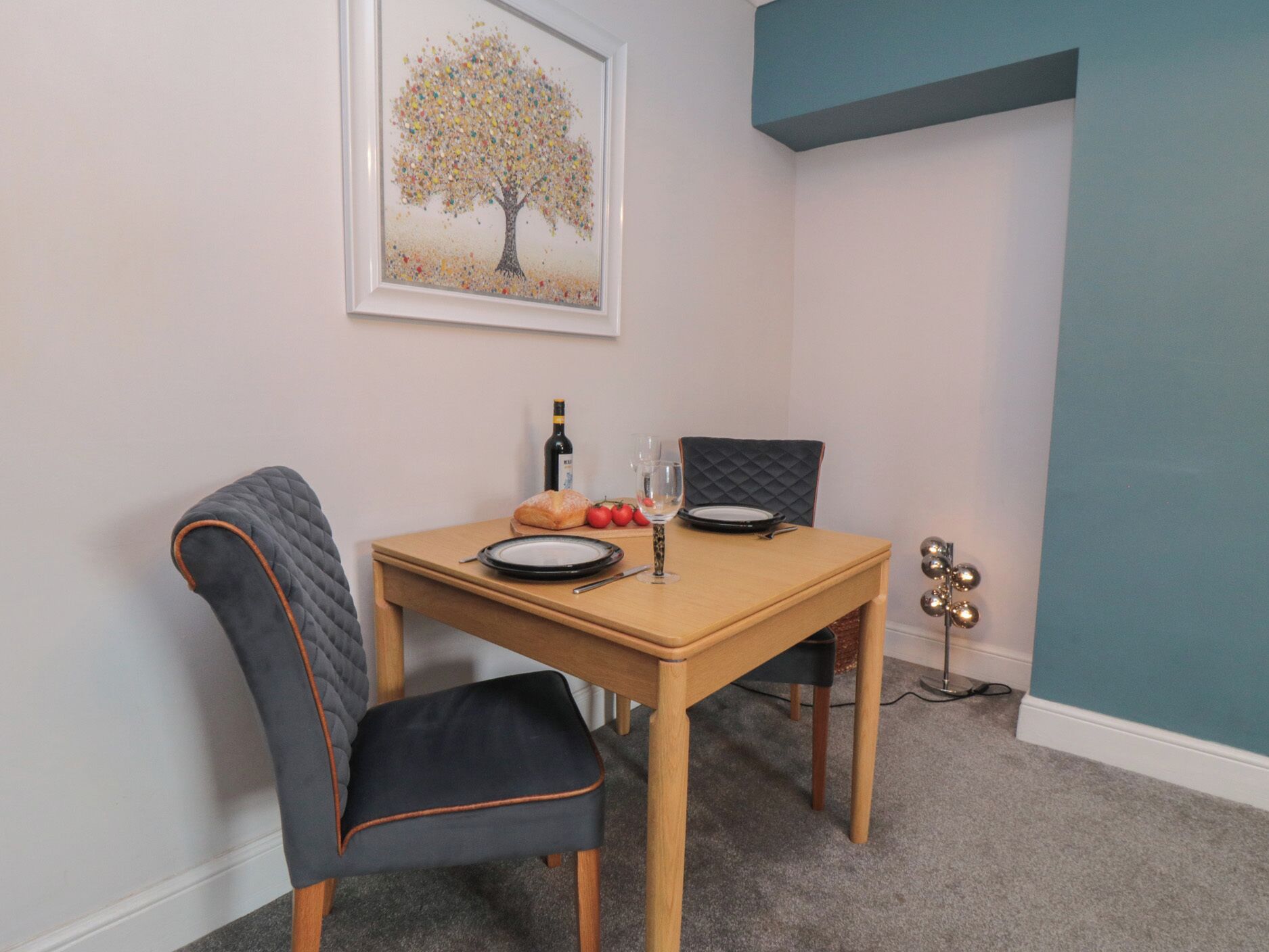 A dining area with a table, chairs, a framed picture, and a wine bottle.