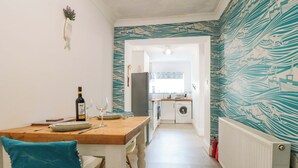 A compact kitchen with a washing machine, a dining table with chairs, and a small refrigerator. - The Hideaway (Whitby)