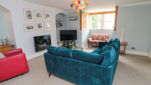 A living room with a teal sofa, a red armchair, a flat-screen TV, and a chandelier. - The Hideaway (Whitby)