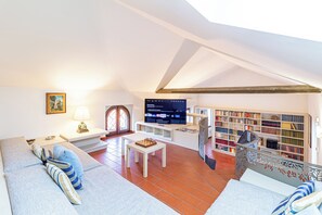 A cozy loft apartment with a high ceiling, a large TV, a bookshelf, and a comfortable seating area.