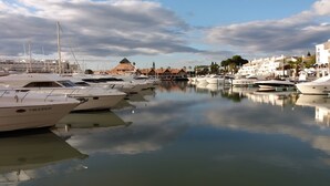 Een jachthaven met diverse jachten afgemeerd, kalm water en gebouwen op de achtergrond.