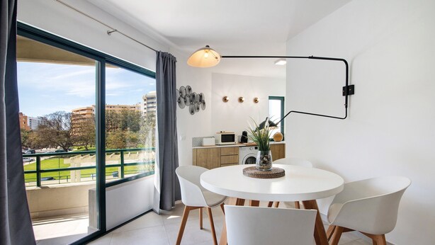 Een moderne eetruimte met een ronde tafel, witte stoelen en een stadsgezicht door grote ramen.