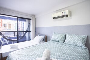 Ein Hotelzimmer mit Bett, einem Fenster mit Blick auf Gebäude, einer Klimaanlage und einer Hängematte.