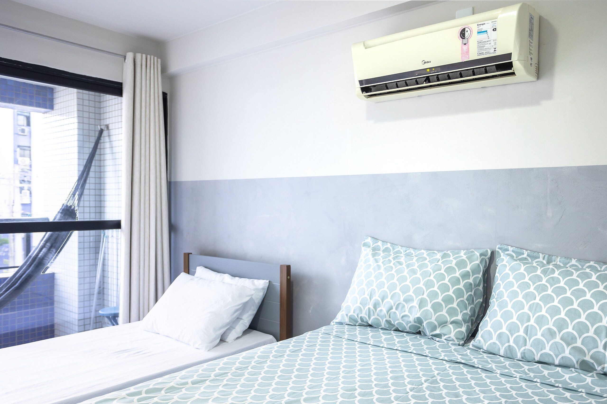A hotel room with a bed, a window with curtains, and an air conditioning unit on the wall.