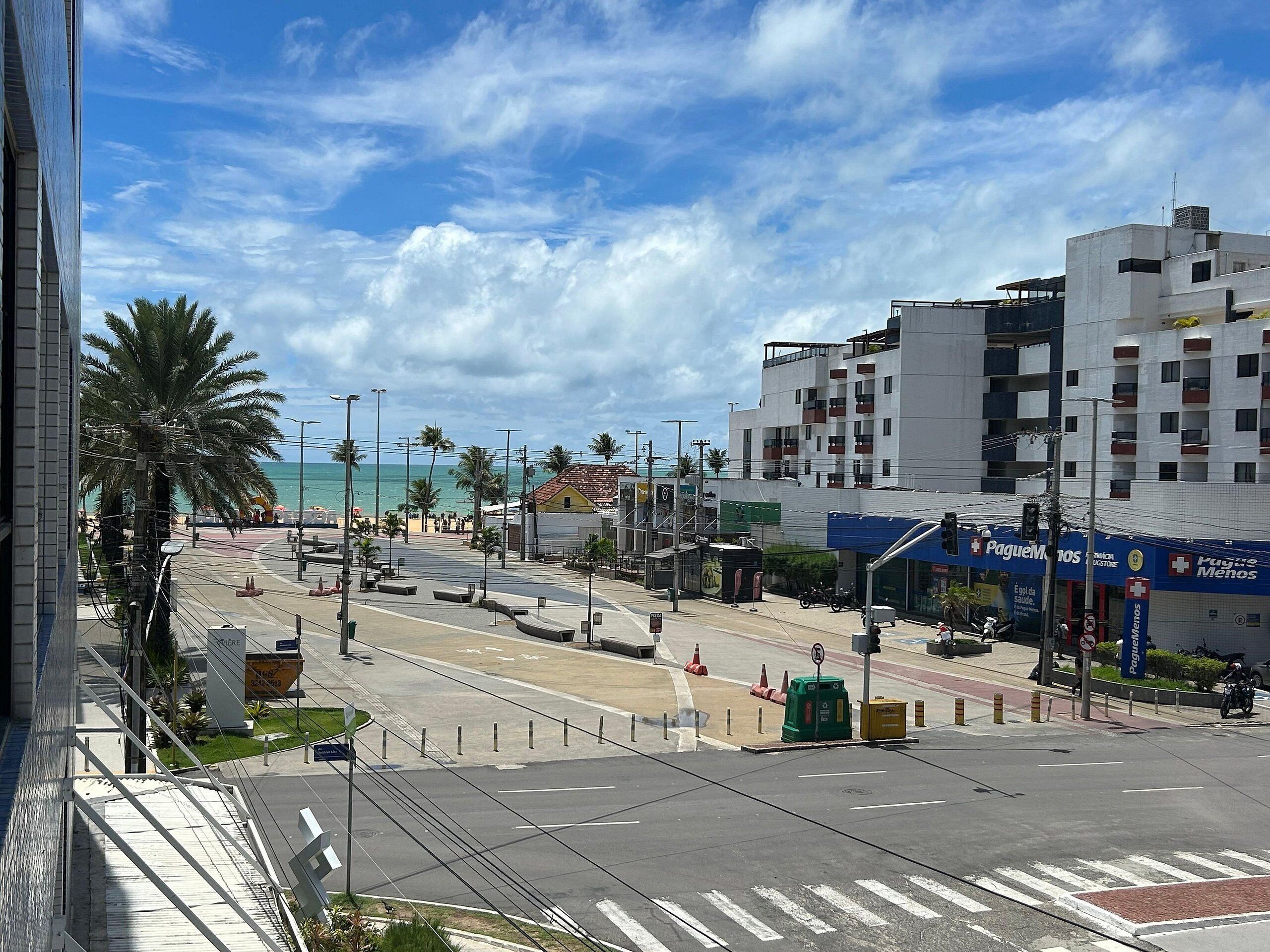 A street view with a beach in the background, palm trees, and a building with a blue awning.