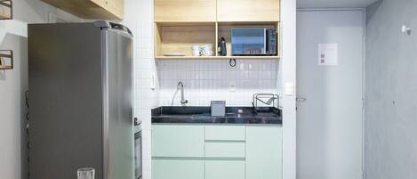 Une cuisine de taille réduite, équipée d’un réfrigérateur, d’un four à micro-ondes et de meubles de couleur verte.