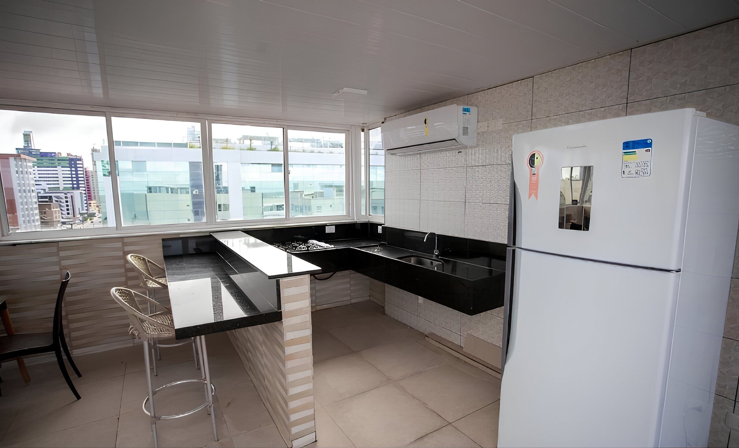 A modern kitchen with a black countertop, white refrigerator, and large windows offering a city view.