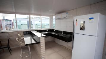 A modern kitchen with a black countertop, white refrigerator, and large windows offering a city view.