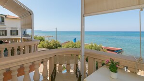 Un balcon donnant sur la mer, une table avec un pot de fleurs et un bâtiment en arrière-plan.