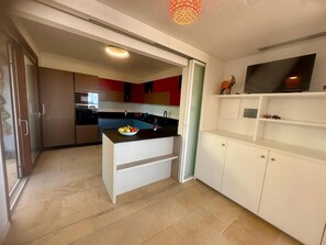 Eine moderne Küche mit einer zentralen Kochinsel, weißen Schränken und einem eingebauten TV-Schrank.