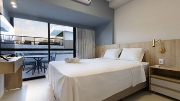 Una habitación de hotel moderna con una cama grande, un escritorio y un balcón con mobiliario exterior.