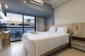 Ein modernes Hotelzimmer mit einem großen Bett, einem Schreibtisch und einem Balkon mit Sitzgelegenheit.