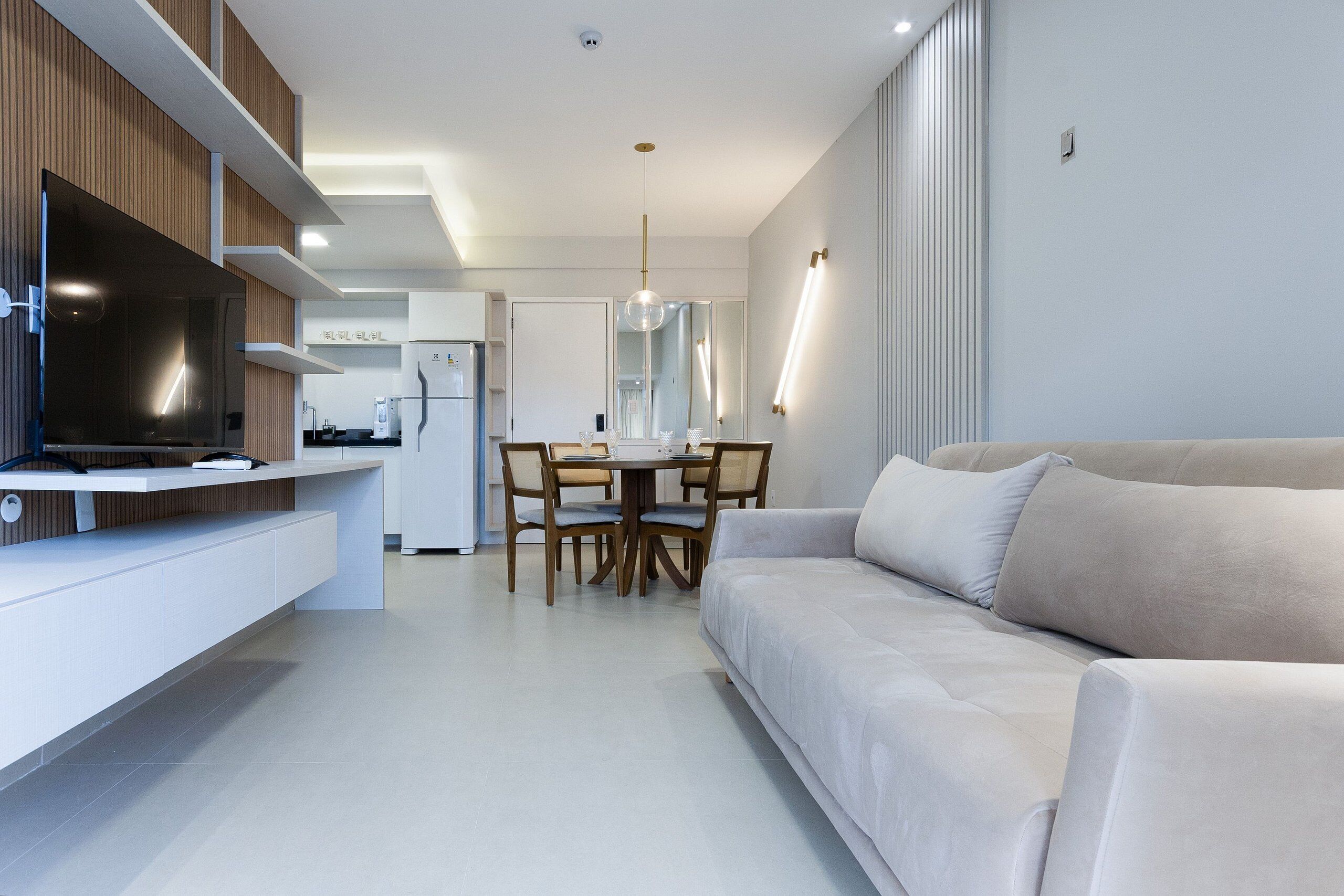 A modern living room with a sofa, a dining area with a table and chairs, and a kitchen area with a TV and cabinets.
