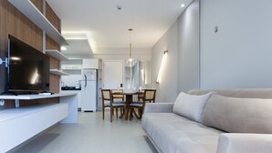 Una sala moderna con un sofá, un comedor con mesa y sillas, y una cocina con televisor y armarios.