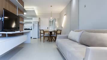 A modern living room with a sofa, a dining area with a table and chairs, and a kitchen area with a TV and cabinets.