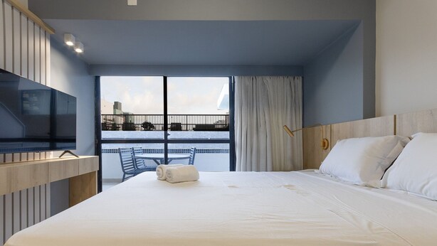 Una habitación de hotel con una cama grande, un televisor, un balcón con vistas y una ventana con cortinas.