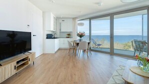 A modern kitchen with white cabinets and a large TV. There is a dining area with a table and chairs, and a large window offering a view of the ocean. - Stunning Seaview Retreat for 4 in Pobierowo (Pobierowo)