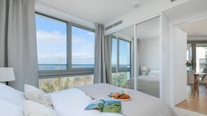 A modern hotel room with a large bed, a view of the sea, and a dining area visible through an open door. - Stunning Seaview Retreat for 4 in Pobierowo (Pobierowo)