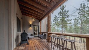 Un terrazzo in legno con posti a sedere all'aperto e un barbecue, affacciato su una zona boschiva.