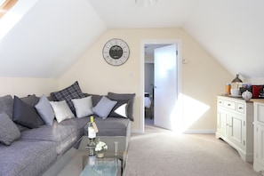 A cozy living room with a grey sofa, a glass coffee table, and a wall clock.