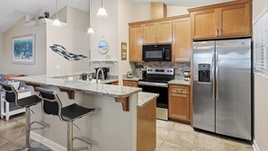 Una cocina con gabinetes de madera, un refrigerador de acero inoxidable, un microondas, una estufa y una barra con taburetes.